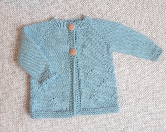 May include: A light blue knitted cardigan with wooden buttons. The cardigan has a simple design with a ribbed texture and a slightly flared hem.