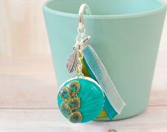Bookmark Peacock feather macaron decorated with gold leaf and golden pearl blue mounted on silver support with matching ribbons and charm