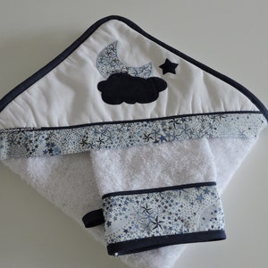 Peut inclure: Serviette à capuche blanche avec une bordure à imprimé étoiles bleu et blanc. La capuche présente un nuage noir avec une lune croissante bleue et une étoile.