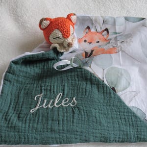 May include: A green and white baby blanket with a crocheted fox toy. The blanket has a white border and the name "Jules" embroidered on it.