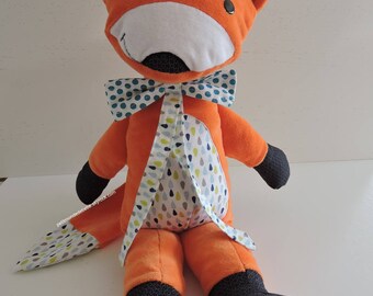 May include: A plush orange fox toy with black eyes, a white nose, and a blue and white polka dot bow tie. The fox is sitting with its legs outstretched and has a blue and white polka dot pattern on its feet.