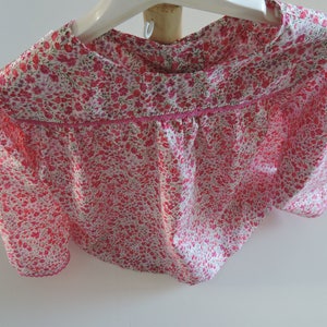 Könnte beinhalten: Eine rosa-weiße Bluse mit Blumendruck, Rüschenkragen und kurzen Ärmeln.