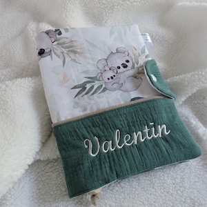 Peut inclure: Une couverture de livre en tissu vert et blanc avec un motif de koala et le nom "Valentin" brodé sur le devant.
