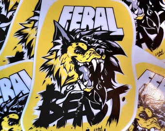 May include: A yellow sticker featuring a black and white illustration of a snarling wolf with the text "FERAL BEAST" in white lettering. The sticker has a black and white splatter pattern around the wolf.