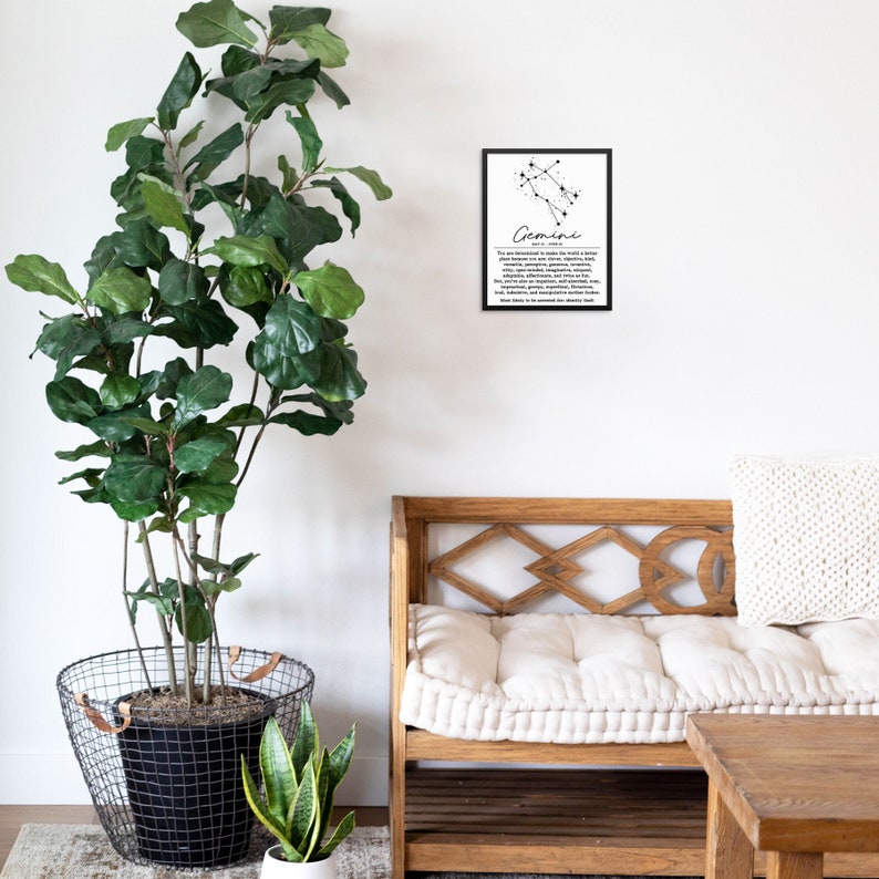 May include: Black and white printable wall art featuring the Gemini constellation with a description of the zodiac sign. The print is framed and hanging on a white wall above a wooden bench with a white cushion.