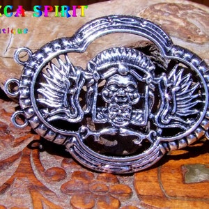 Può includere: Ciondolo in metallo argentato con un design dettagliato di un viso stilizzato con ali. Il ciondolo ha tre anelli per attaccarlo a una collana o un braccialetto. Il ciondolo è su una superficie di legno.