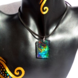 May include: A black suede cord necklace with a rectangular iridescent pendant featuring swirling colours of blue, green, red, and gold. The pendant is made of resin and has a shiny, glossy finish.