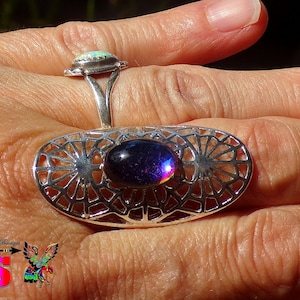 May include: Two silver rings featuring colourful gemstones. The top ring has a white opal gemstone. The bottom ring has a large, oval-shaped, iridescent gemstone with a silver filigree design.