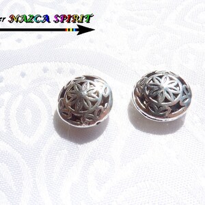 Pode incluir: Duas contas de metal prateado com um design floral decorativo e intrincado. As contas são redondas e têm um furo no centro para enfiar.