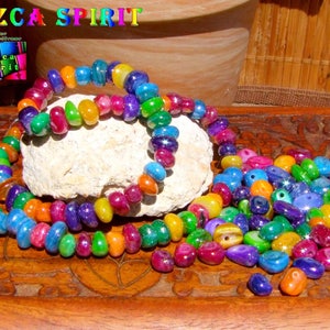 Può includere: Una collana di perline di vetro iridescente colorate in varie tonalità di blu, verde, rosso, arancione e viola. Le perline sono disposte in cerchio e si trovano su una superficie di legno.