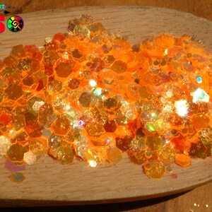 Peut inclure: Gros plan sur des paillettes orange irisées sur une cuillère en bois. Les paillettes sont de forme hexagonale et de tailles variées.
