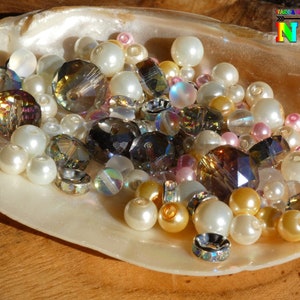 Peut inclure: Un assortiment de perles dans une coquille de coquillage, y compris des perles claires, irisées, dorées et roses.