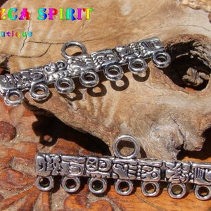 Könnte beinhalten: Zwei silberfarbene Metall-Verbindungsanhänger mit filigranen Designs und mehreren Schlaufen. Die Anhänger zeigen ein sich wiederholendes Muster aus stilisierten Figuren und Symbolen.