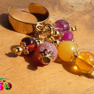 Op de afbeelding: Gouden verstelbare ring met een hangende bedel met verschillende gekleurde edelsteen kralen, waaronder paarse, roze, gele en oranje.