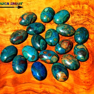 Könnte beinhalten: Eine Sammlung von 15 ovalen Türkis-Cabochons mit braunen und goldenen Einschlüssen. Die Cabochons sind auf einer Holzoberfläche angeordnet.