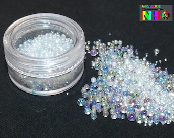 May include: A small clear jar filled with iridescent white glass beads. The jar is sitting on a black surface and there are more beads scattered around it.