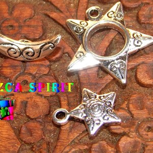 Puede incluir: Tres abalorios de metal plateado con diseños intrincados. Un abalorio de media luna, un abalorio de estrella con un agujero en el centro y un abalorio de estrella más pequeño.