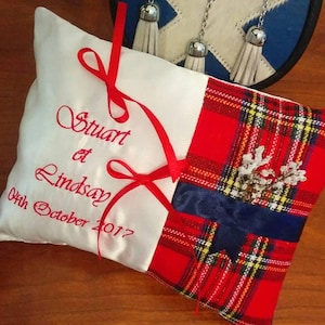 Peut inclure: Un coussin d'alliance en satin blanc avec un ruban rouge et un panneau de tissu tartan rouge, bleu et jaune. Le coussin est brodé avec le texte "Stuart & Lindsay 04th October 2017".