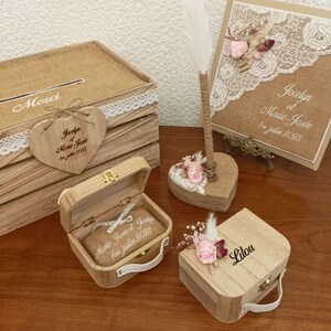 Peut inclure: Ensemble de décorations de mariage rustiques. Comprend une boîte en bois avec le texte "Merci", une étiquette en forme de cœur, une boîte à alliances, un porte-plume et un livre d'or. Tous les articles ont des accents de toile de jute et de dentelle, avec des ornements floraux et de plumes.