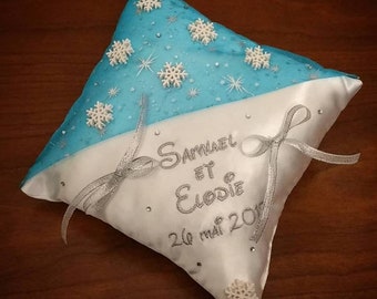 May include: White satin pillow with blue satin trim and snowflake embellishments. The pillow is embroidered with the names "Sammael et Elodie" and the date "26 mai 2017".