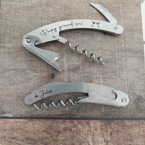 May include: Two silver-colored bottle openers with corkscrews. The top opener has the text "Papy grand cru" and a graphic of two wine glasses clinking. The bottom opener has the text "de Jules".