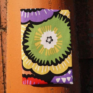 May include: A fabric pouch with a colorful floral pattern. The pattern features large, stylized flowers in shades of green, yellow, purple, and red.