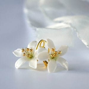 Peut inclure: Deux fleurs en porcelaine blanche avec des accents dorés, attachées à un fil de fer doré, sur un fond blanc.