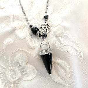 Könnte beinhalten: Schwarze und silberne Halskette mit einem schwarzen Kristallpendel, einem silbernen Pentagramm-Anhänger und schwarzen und silbernen Perlen.
