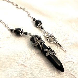 May include: Black onyx pendulum with a silver chain and a silver leaf design. The pendulum is attached to a silver bird skull charm.