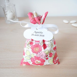 May include: A white fabric bag with a pink floral pattern and a white tag that says "Agathe 25 aout 2018". The bag is tied with a white ribbon.