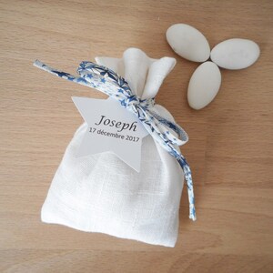 May include: White linen favor bag with a blue and white patterned ribbon tied around it. A white star-shaped tag is attached to the ribbon with the text "Joseph 17 d&eacute;cembre 2017".