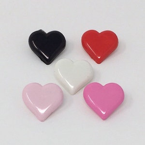 Könnte beinhalten: Fünf herzförmige Knöpfe in verschiedenen Farben: Schwarz, Rot, Weiß, Rosa und Hellrosa.