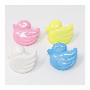 May include: Four plastic duck buttons in pink, yellow, white, and blue. The buttons are shaped like ducks with a raised wing design.