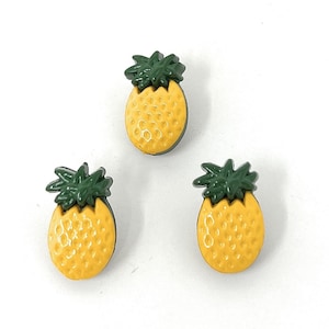 Könnte beinhalten: Drei gelbe Ananas-Knöpfe mit grünen Blättern.