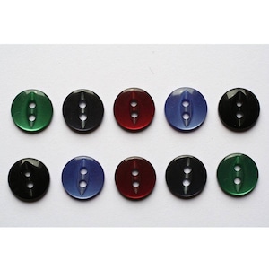 Könnte beinhalten: Zehn runde Plastikknöpfe mit jeweils zwei Löchern. Die Knöpfe sind in verschiedenen Farben, darunter grün, blau, rot und schwarz.