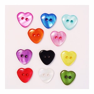 Puede incluir: Doce botones en forma de corazón de varios colores, incluyendo rosa, azul, verde, amarillo, rojo, negro y blanco. Cada botón tiene dos agujeros.