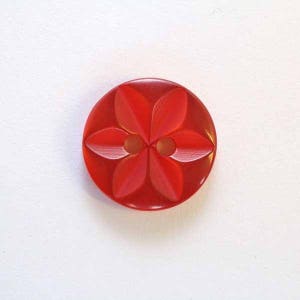 May include: A red plastic button with a four-petal flower design. The button has two holes.