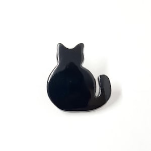 May include: Black enamel cat silhouette pin. The pin is shaped like a cat sitting with its tail curled around its body.