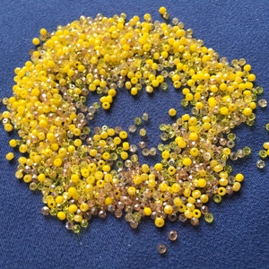 May include: A large pile of yellow and clear glass beads. The beads are small and round, and they are scattered on a blue surface.