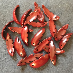 Puede incluir: Una colección de 17 cuentas de madera talladas de color rojo con forma de hoja. Las cuentas tienen un acabado liso y pulido y son perfectas para la elaboración de joyas o manualidades.