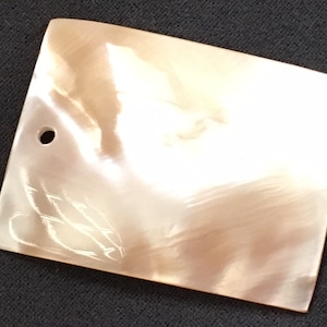 Peut inclure: Une pièce rectangulaire de nacre blanche et irisée avec un petit trou percé en haut.