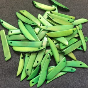 May include: A pile of green, leaf-shaped, shell beads with two holes in each bead. The beads are smooth and have a slight sheen.