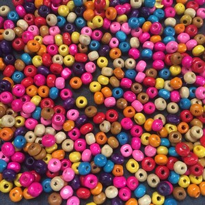 May include: A large assortment of colorful wooden beads. The beads are round and have a hole in the center. The beads are in various shades of pink, blue, yellow, orange, red, brown, and purple.