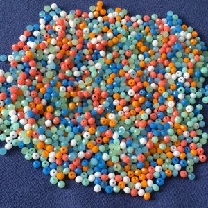 May include: A large pile of colorful glass beads in shades of blue, green, orange, and white. The beads are faceted and have a shiny finish.