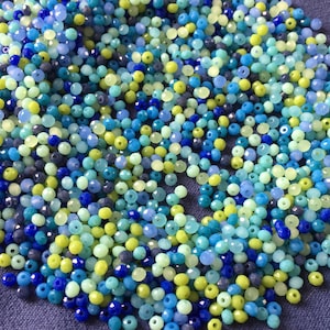 May include: A large assortment of small, faceted glass beads in shades of blue, green, and yellow. The beads are perfect for jewelry making or other craft projects.