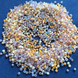 May include: A large assortment of small, round, glass beads in various shades of purple, pink, yellow, and white.