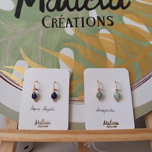 Peut inclure: Deux paires de boucles d'oreilles pendantes dorées présentées sur des cartes blanches. Une paire comporte des pierres en forme de goutte Lapis Lazuli bleu foncé, l'autre des pierres Amazonite vert clair. Chaque carte porte le nom de la pierre et Malicia Creations.