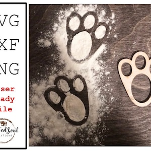 May include: A wooden paw print cutout next to paw prints made in flour on a dark wood surface. The image includes the text "SVG, DXF, PNG, Laser Ready File" and the Blessed Soul Creations logo.