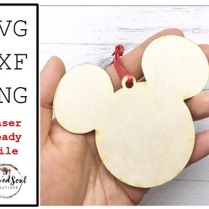 Op de afbeelding: Een houten Mickey Mouse-vormig ornament met een rood lint om op te hangen. Het ornament wordt in een hand gehouden. Tekst aan de linkerkant luidt "SVG, DXF, PNG, Laser Ready File" en "Blessed Soul Creations".
