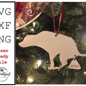 Può includere: Un ornamento natalizio in legno a forma di cane con un piccolo tag che recita "2020". L'ornamento è appeso a un albero di Natale. Il testo "SVG, DXF, PNG, Laser Ready File" è sul lato sinistro.